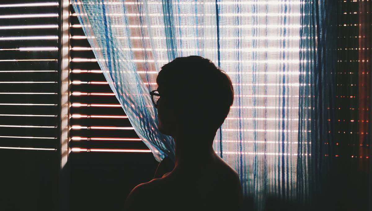 window person with eyeglasses staring at opened window curtain